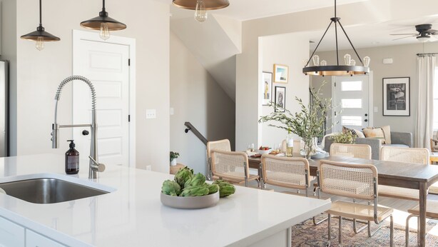 Een moderne keuken met een centraal eiland, een roestvrijstalen spoelbak en hangende lampen.