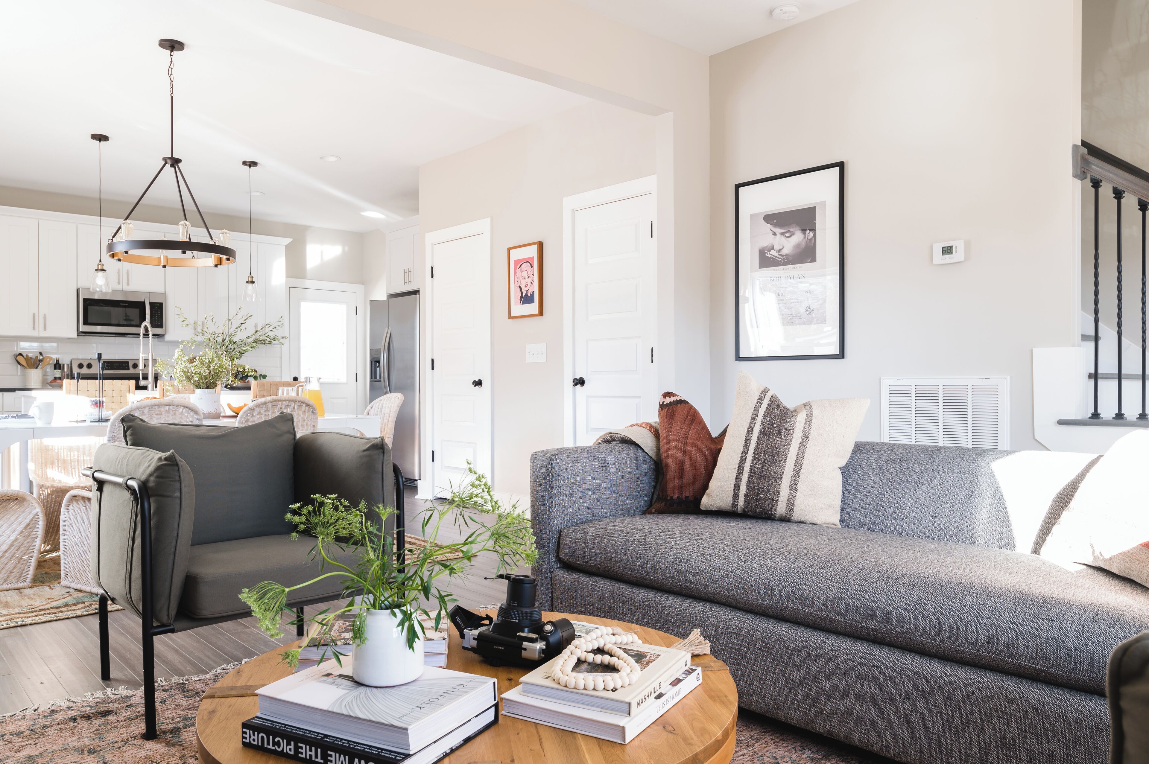A modern living room with a grey sofa, a coffee table with books and a camera, and a dining area in the background.