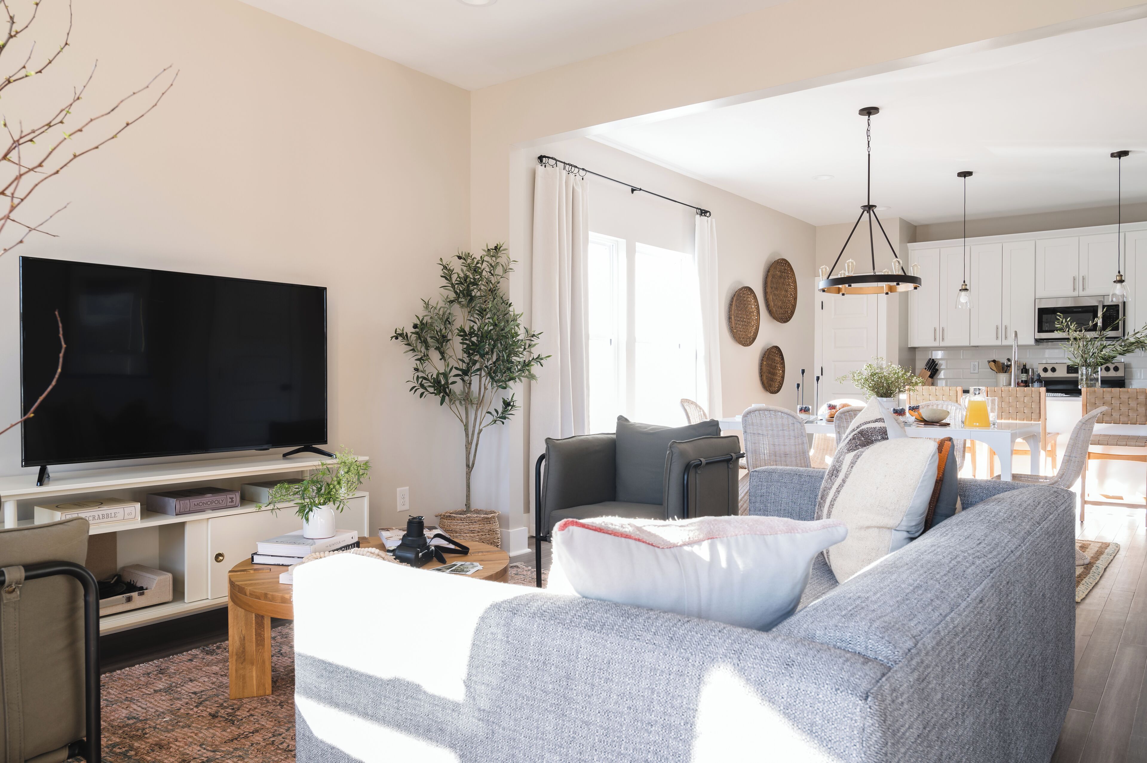 Una sala de estar moderna con televisor de pantalla plana, sofá gris y comedor, con una cocina al fondo.