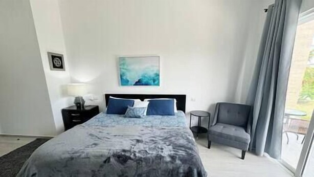 A hotel room with a large bed, a bedside table, a chair, and a window with curtains.