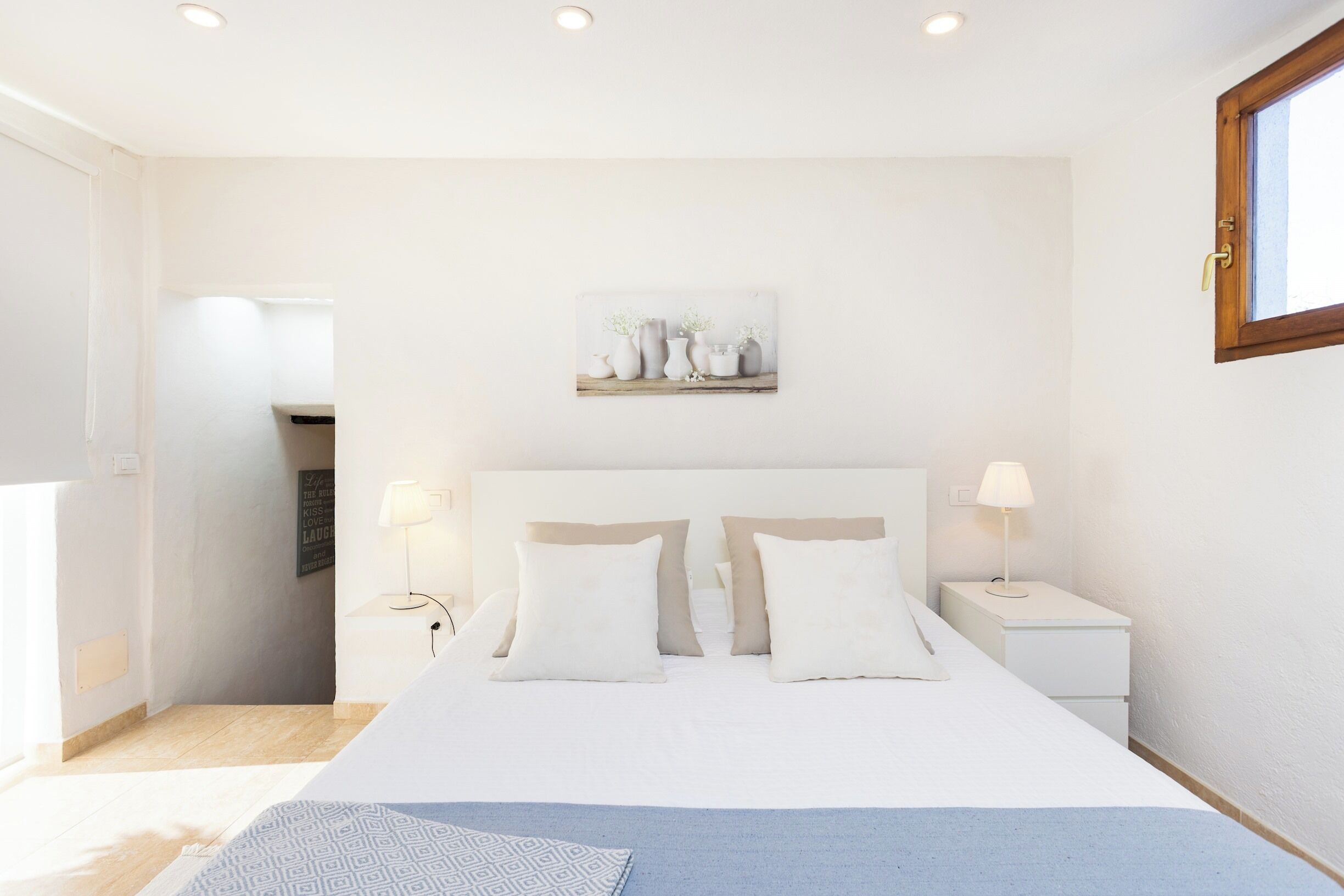 A bedroom with a large bed, two bedside tables, a nightstand, and a wall-mounted artwork.