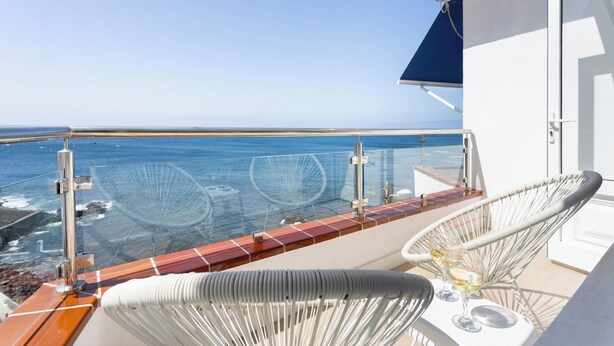 A balcony with a view of the ocean, a white chair, and a table with a glass of wine. - Home2Book Luminous Seaviews Apt Near The Ocean (Punta del Hidalgo)