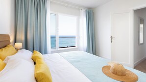A hotel room with a bed, a view of the sea through a window, and a door to the right. - Home2Book Luminous Seaviews Apt Near The Ocean (Punta del Hidalgo)