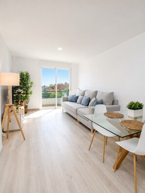 Una sala de estar moderna con una mesa de vidrio, sofá blanco y un balcón con vistas.