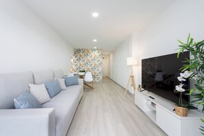 A modern living room with a grey sofa, a flat-screen TV, and a dining area in the background. - Home2Book Relaxing Poolside Escape, Arona (Adeje)