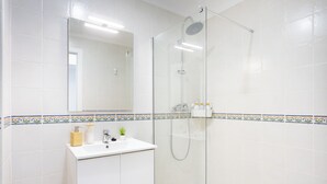 Een moderne badkamer met een douchecabine van glas, een witte wastafel met spiegel erboven en decoratieve tegels langs de plint.