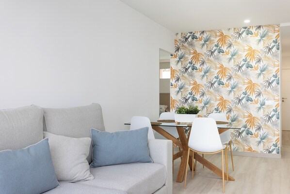 A modern living room with a grey sofa, white chairs, and a glass dining table.