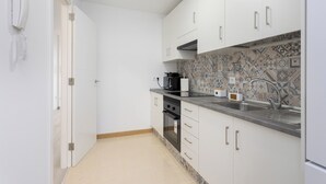 Een kleine keuken met witte kastjes, een inbouwoven, een magnetron en een decoratieve spatelwand.