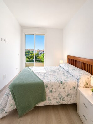 A bedroom with a bed, a nightstand, a green throw blanket, and a view of greenery and buildings through a sliding door. - Home2Book Relaxing Poolside Escape, Arona (Adeje)