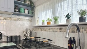 Ett kök med en svart diskho, en blandare i rostfritt stål och en kakelbeklädd vägg bakom diskbänken. Det finns hyllor med dekorativa föremål och krukväxter.