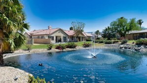Zona residencial con piscina, fuente y casas con césped cuidado y palmeras.