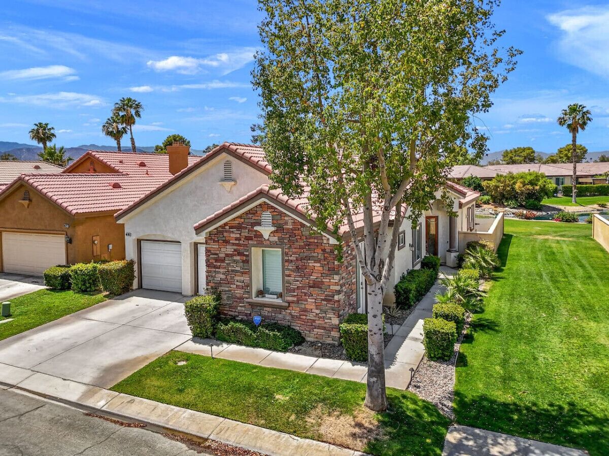 A residential neighborhood with houses featuring red-tiled roofs, stone facades, and well-maintained lawns.