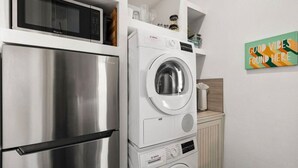 Una cocina compacta con un refrigerador de acero inoxidable, una lavadora Bosch y un microondas.