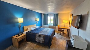 A hotel room with a bed, bedside lamps, a desk with a chair, a television, and a window with curtains. - MetroParc 'nSuites (Stockton)