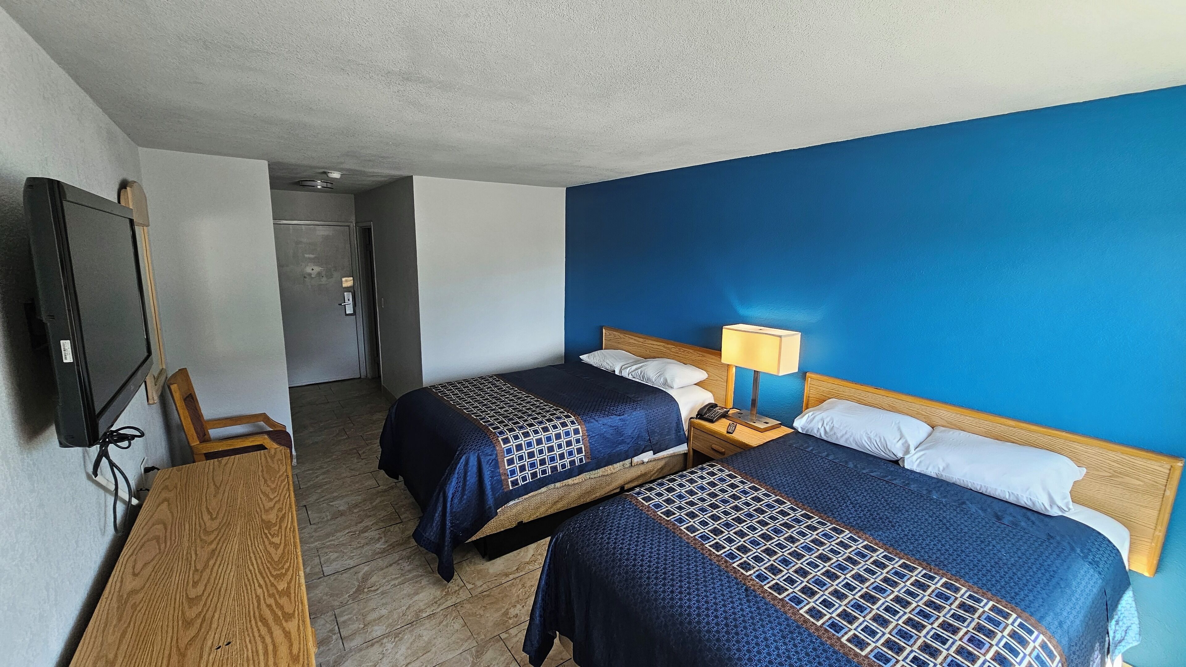 Una habitación de hotel con dos camas, televisión, escritorio y lámpara.