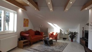 A spacious living room with a sloped ceiling, a red sofa, a coffee table, and a television. - Excl. Apartment for the discerning, 75 sqm, attic, 2 pers. (Heeßen)