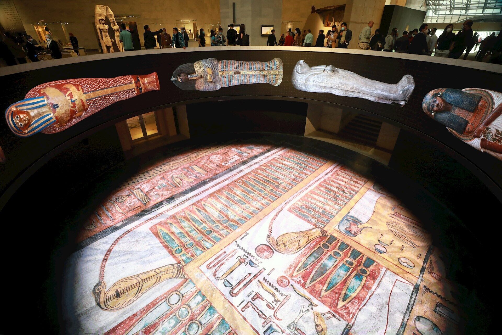 Una exposición de museo con sarcófagos del antiguo Egipto y un gran mural.