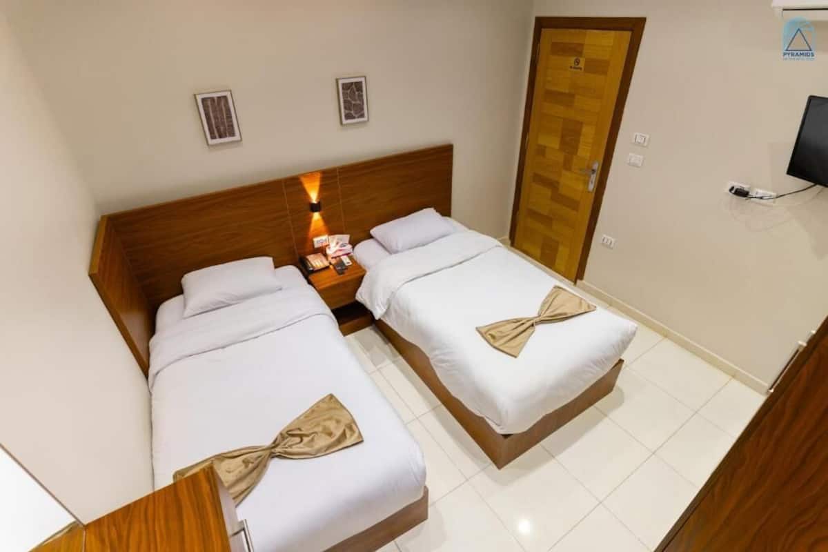 A hotel room with two beds, a wooden headboard, a nightstand with a lamp, a television, and a door with a wooden panel.