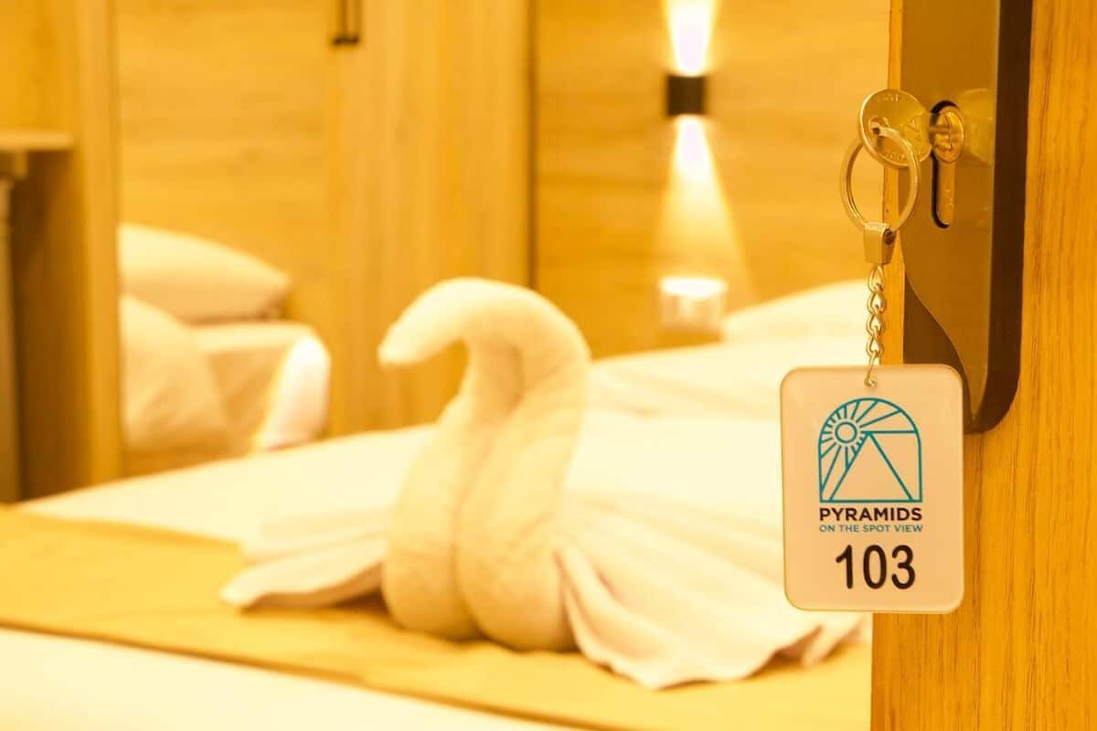 A hotel room with a swan-shaped towel on the bed, a keychain with a hotel logo, and a room number sign.
