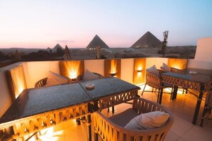 A terrace with a table and chairs, a view of pyramids, and a clear sky. - Pyramids On The Spot View (Giza)