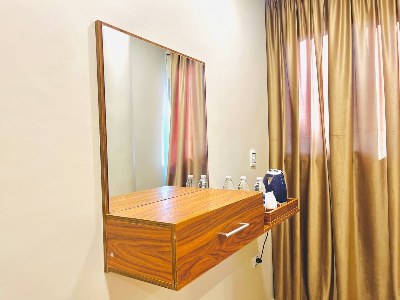 A wooden vanity with a mirror, a drawer, and a tray with a kettle and bottles.