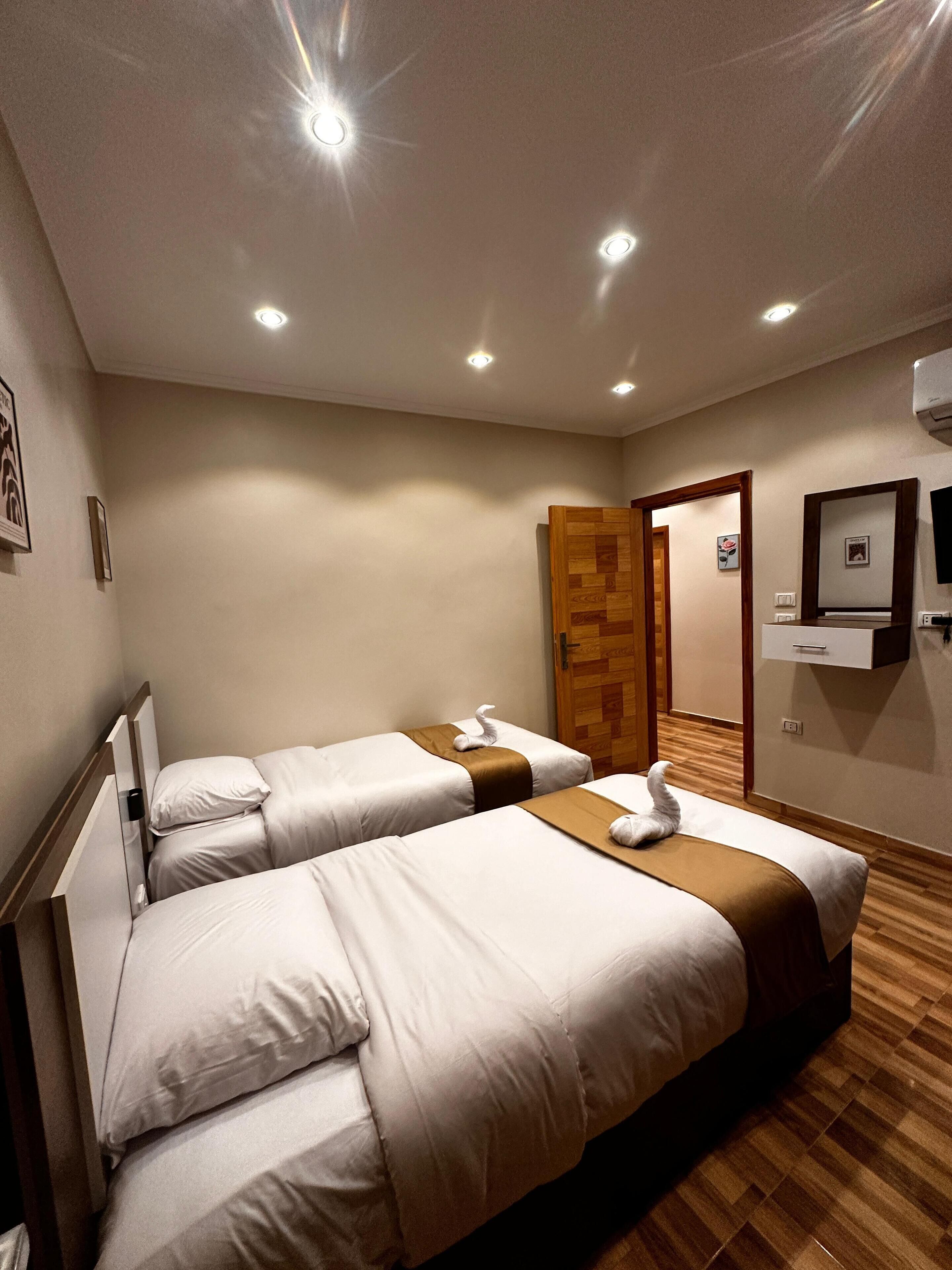 A hotel room with two beds, a wooden door, a flat-screen TV, and a wall-mounted air conditioner.