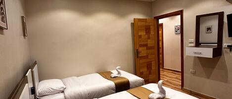 A hotel room with two beds, a wooden door, a flat-screen TV, and a wall-mounted air conditioner.
