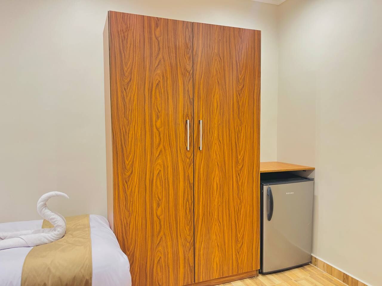 Una habitación con armario de madera, un refrigerador pequeño y una cama con toalla.