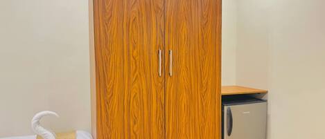 Una habitación con armario de madera, un refrigerador pequeño y una cama con toalla.