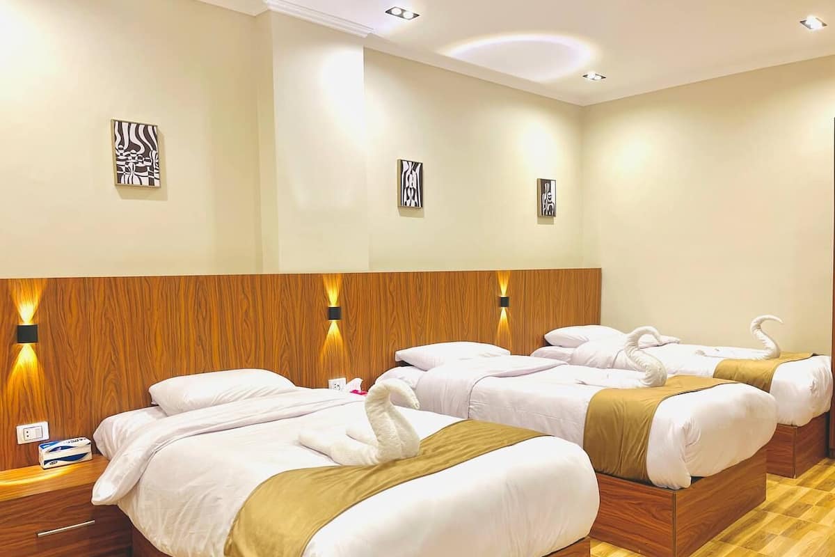 A hotel room with four beds, wooden headboards, and wall-mounted light fixtures.