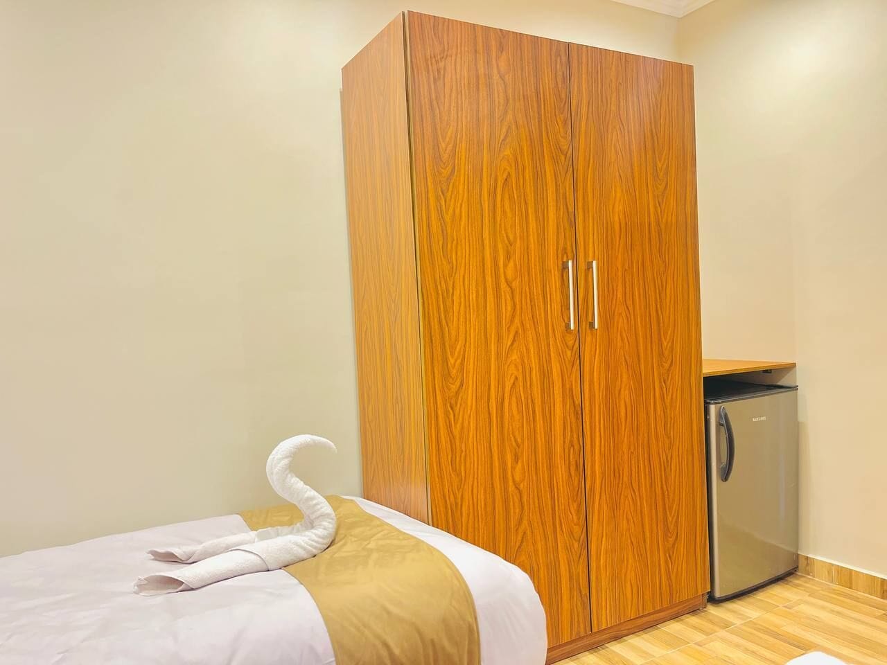 Un dormitorio con un armario de madera, una cama con toallas y un refrigerador pequeño.