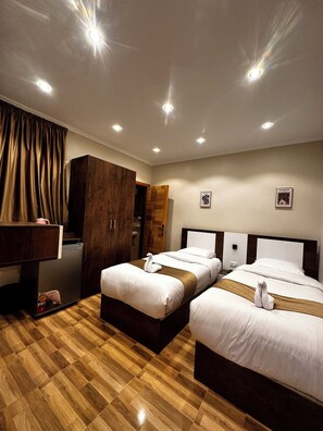 Habitación de hotel con dos camas, un armario de madera, un escritorio con una computadora y un baño visible a través de una puerta abierta.