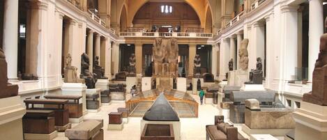 An indoor museum with classical architecture, featuring columns, statues, and a central staircase.