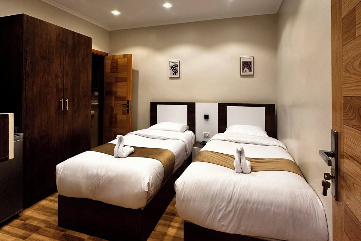 A hotel room with two beds, wooden flooring, and a wardrobe.