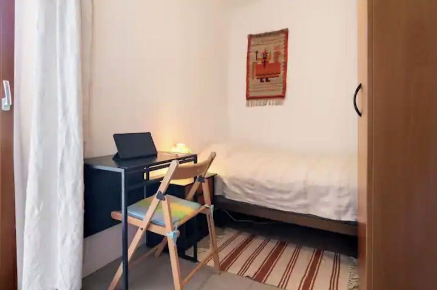Una habitación pequeña con cama, escritorio, computadora portátil, silla y un adorno en la pared.