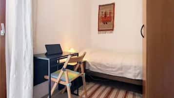 Una habitación pequeña con cama, escritorio, computadora portátil, silla y un adorno en la pared.