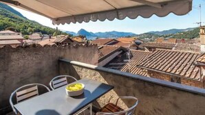 A balcony with a table and chairs, overlooking a mountainous landscape with traditional buildings. - CASA  VISTA (Lugano)