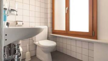 A small bathroom with a white toilet, a sink, and a cabinet above the toilet.