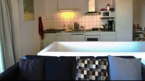 A kitchen with white cabinets, a microwave, and a stove. There is a window with curtains and a red towel hanging on the wall. - CASA  VISTA (Lugano)