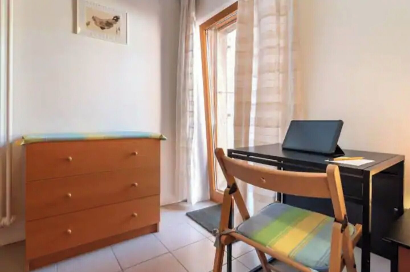 Ein Zimmer mit einem Holzkasten, einem Schreibtisch mit einem Laptop und einem Stuhl.