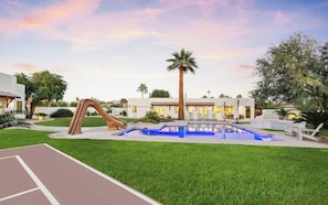 Un'area piscina con scivolo, palme e campo da tennis.