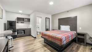 A modern hotel room with a bed, a desk, a microwave, a small kitchenette, and a bathroom. - Southern Suites Forest Park (Forest Park)