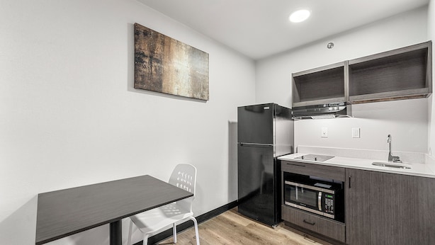 A compact kitchen with a dark countertop, white chair, and a black refrigerator. - Southern Suites Forest Park (Forest Park)