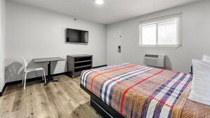 A bedroom with a bed, a desk, a chair, a TV, and a window with blinds. - Southern Suites Forest Park (Forest Park)