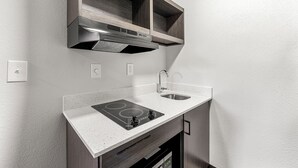 A compact kitchen with a built-in stove, sink, and wooden cabinets. - Southern Suites Forest Park (Forest Park)