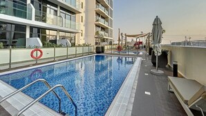 Une piscine sur le toit, avec une eau d’un bleu limpide, entourée d’un bâtiment moderne doté de balcons et d’une bouée de sauvetage.