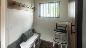 Un pasillo con un banco blanco, un taburete pequeño, un perchero y una ventana con barrotes.