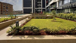 Un edificio moderno con varios balcones y un patio ajardinado con plantas y una pequeña piscina.