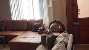 A living room with a brown leather sofa, a wooden coffee table, and a globe. There is a window with blinds and a door with a sign. - ENTIRE Big Family Home Close To Zoo and Events - Private Patio and Firepit (Pittsburgh)