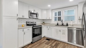 Una cocina moderna con armarios blancos, electrodomésticos de acero inoxidable y un suelo de madera en patrón de espiga.